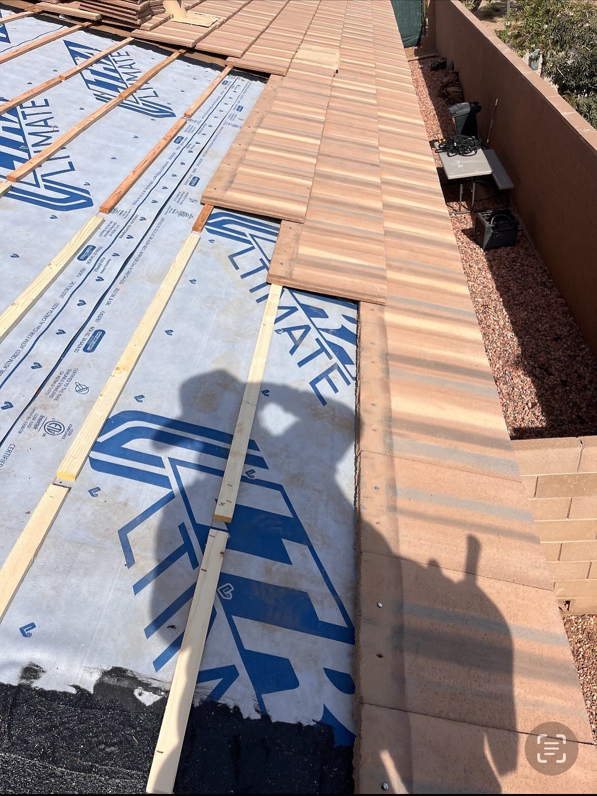 Roofing work in progress: roof tiles being installed over underlayment; shadow of a person.
