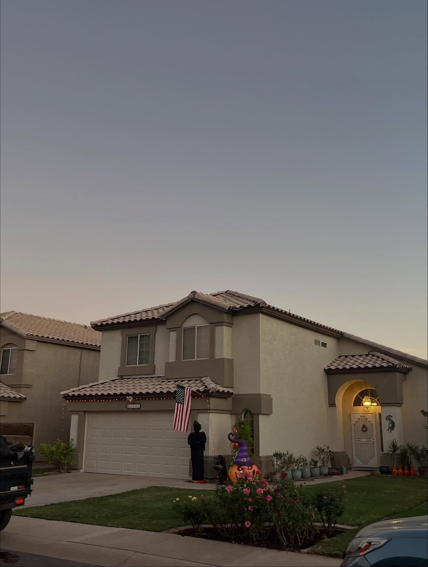 Two-story beige house with Halloween decorations on the lawn; blue sky in the background.