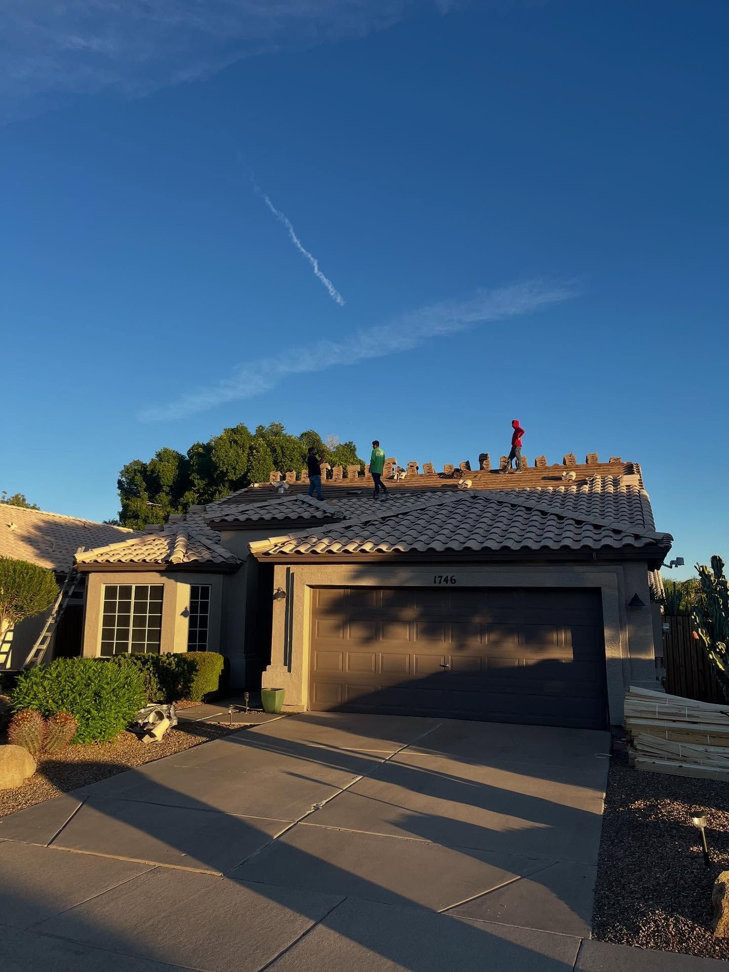 House with construction on roof; workers visible. Blue sky, brown garage door.