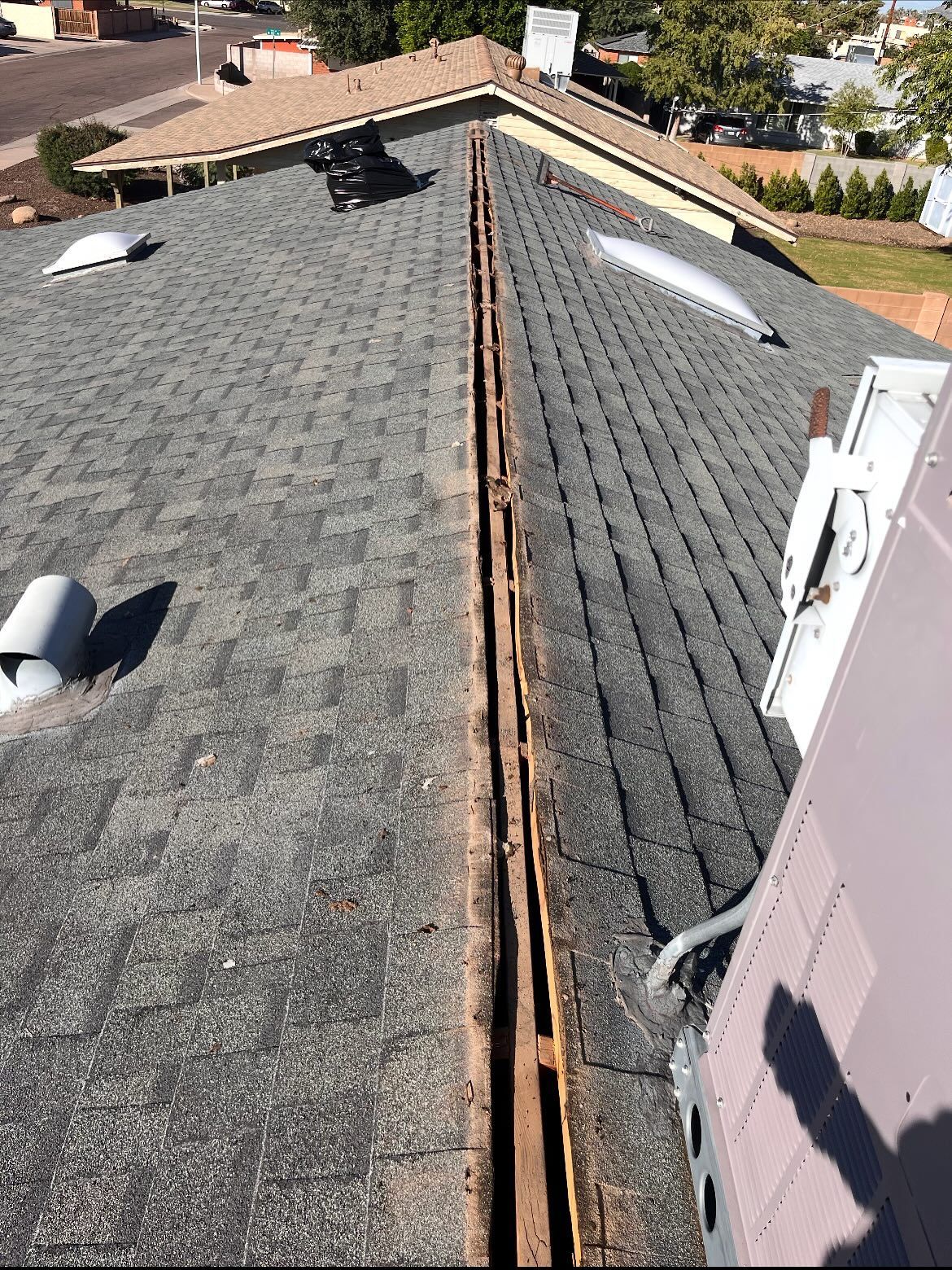 Rooftop with asphalt shingles and a central open gutter; a/c unit visible on the right.