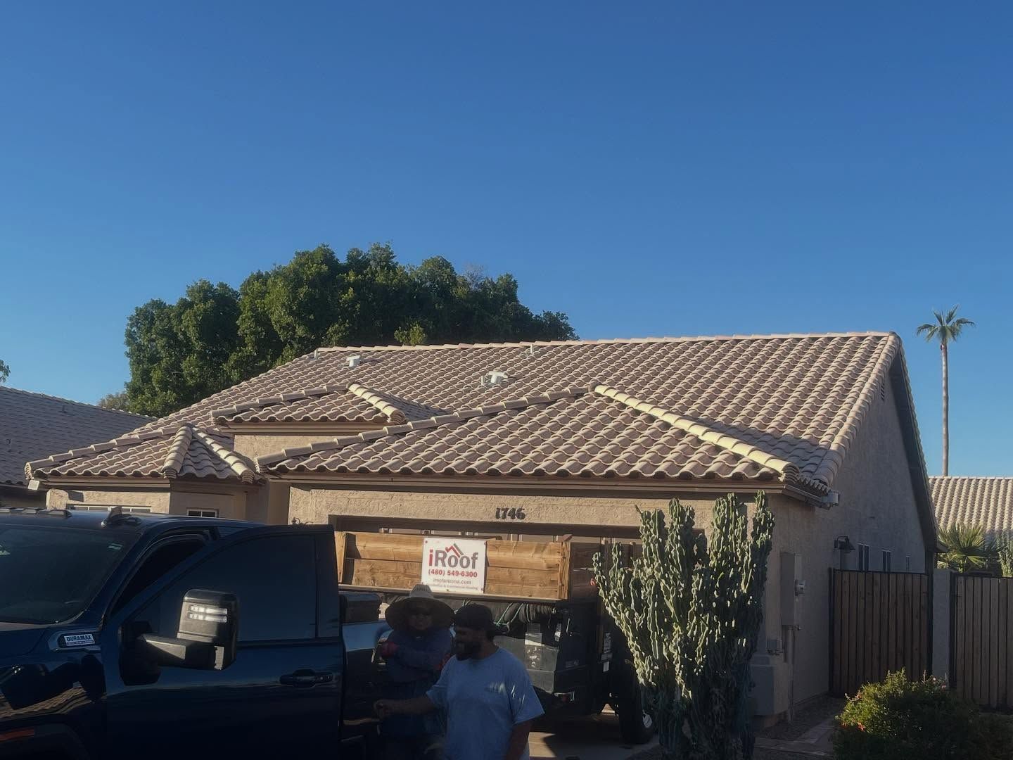 Tan-roofed house with car parked in front, person standing nearby, bright blue sky.