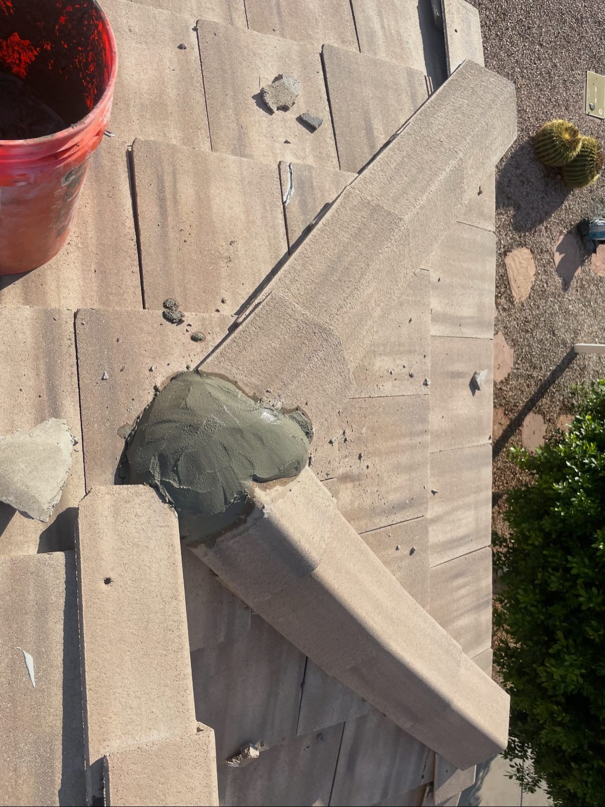 Roof repair: Mortar applied to a section of angled roof tiles, with a bucket and debris visible.