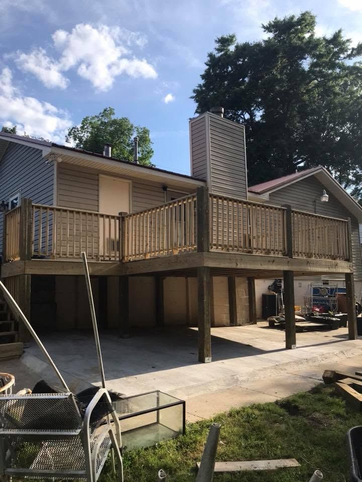 Raised wooden deck attached to a house, with stairs, a brick chimney, and a carport beneath