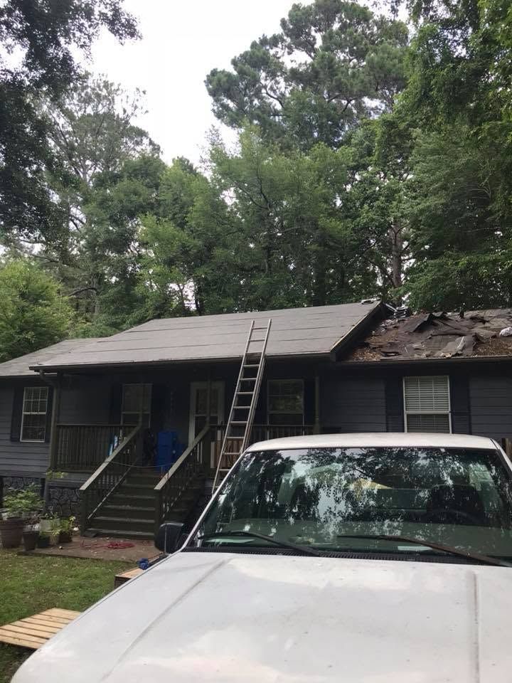 House with damaged roof and ladder, parked white car in front, surrounded by trees