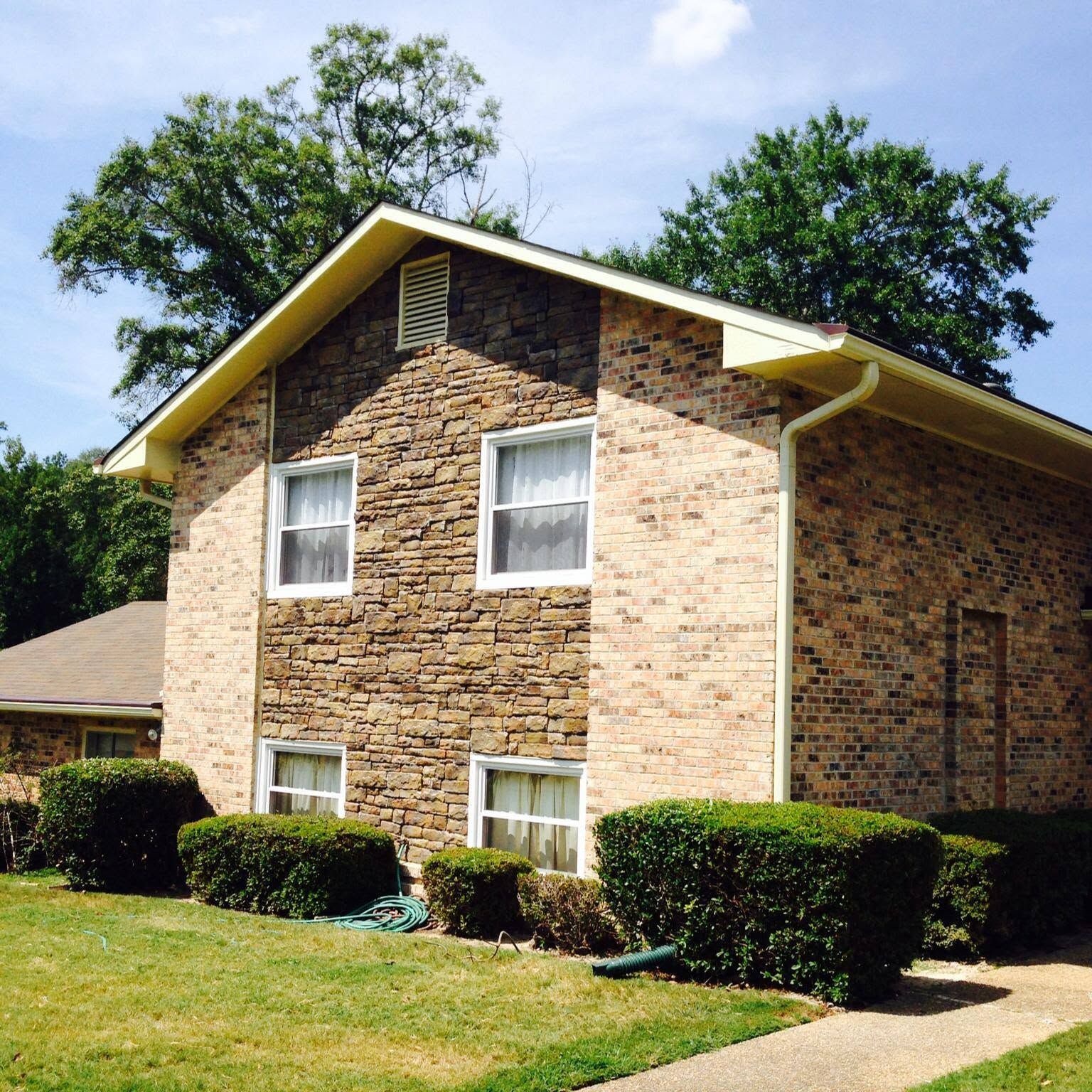 Two-story brick apartment building with white-trimmed windows and trimmed bushes in front