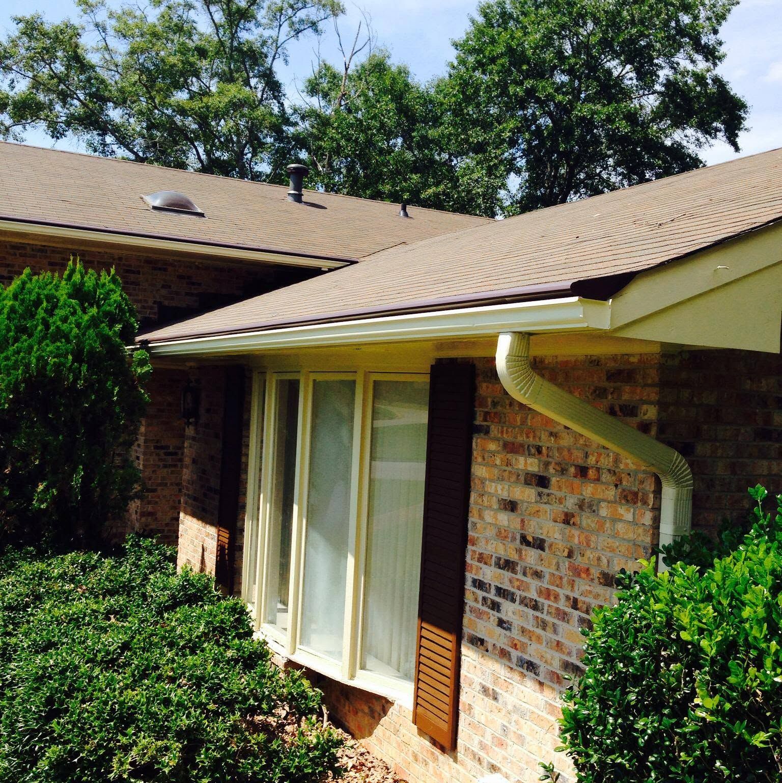 Brick house exterior with tan roof, large windows, and trimmed green shrubs under a bright sky