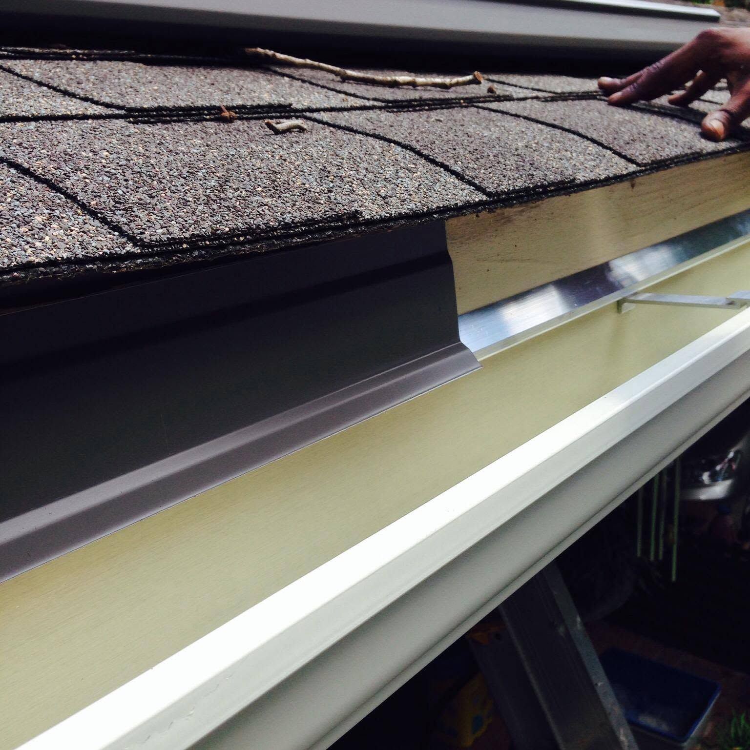 Roof edge with shingles and a metal gutter being installed by a worker’s hand