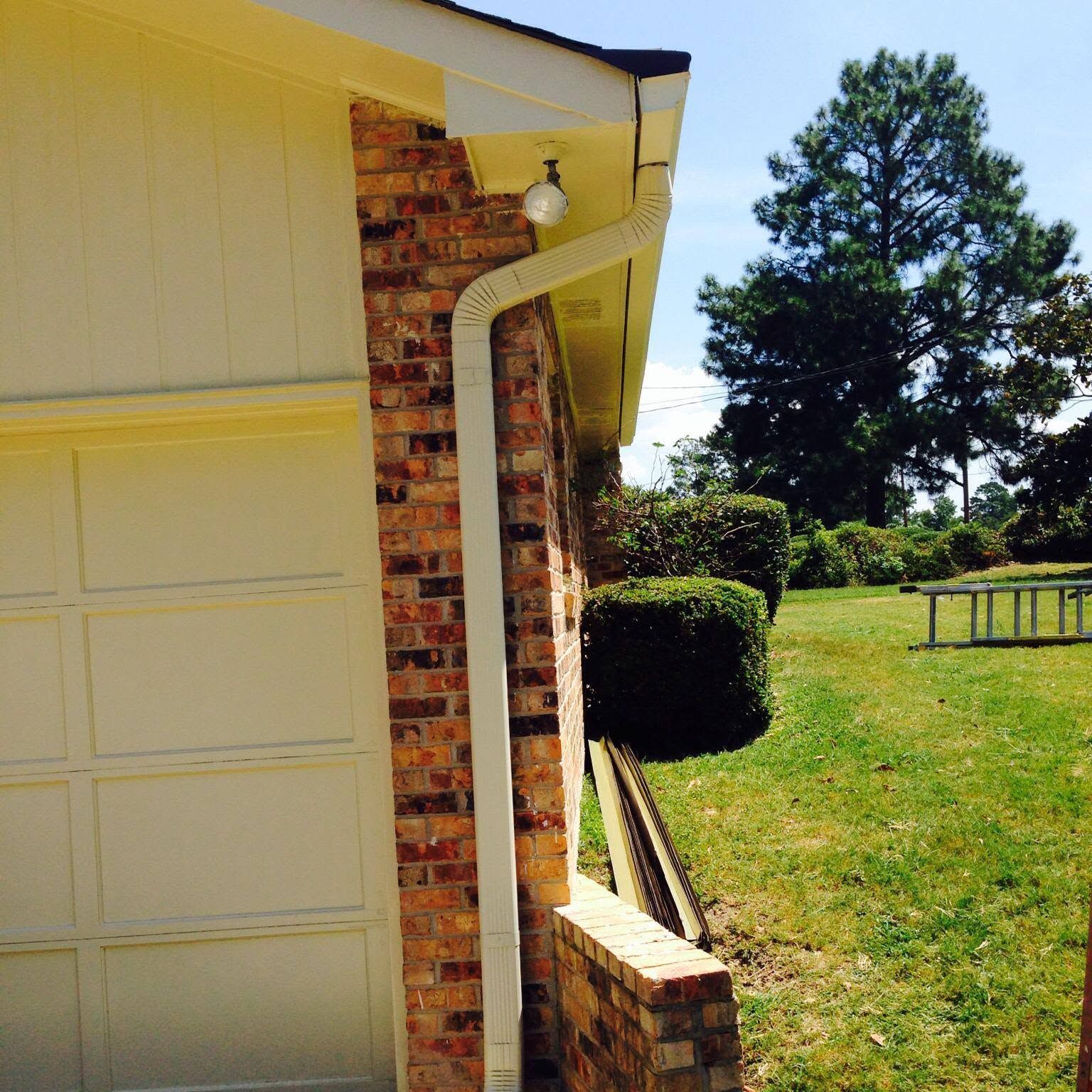 Side of a cream garage and brick house beside a green lawn with trees and a picnic table.