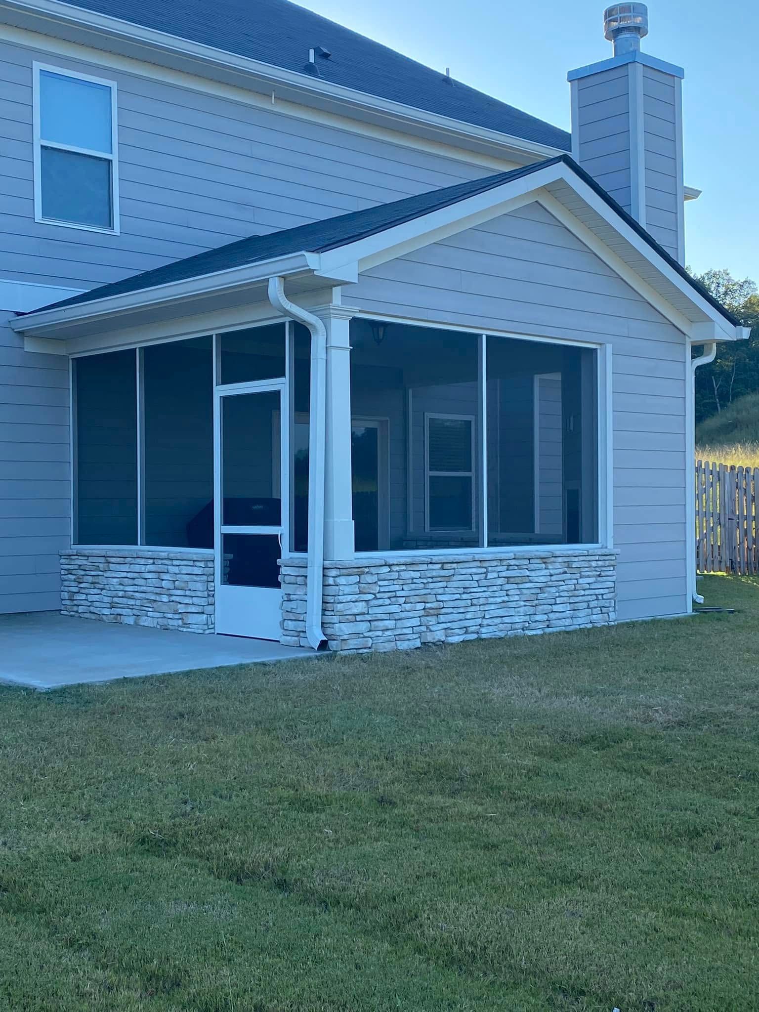 Suburban house with a screened porch, stone base, and grassy lawn at dusk