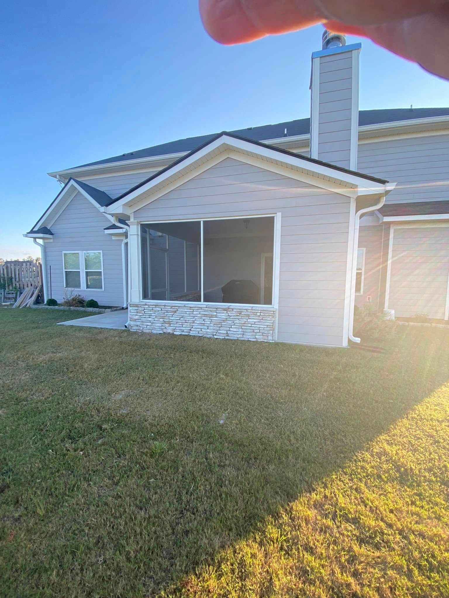 Suburban house with screened porch, white siding, stone base, and chimney in bright sunlight.