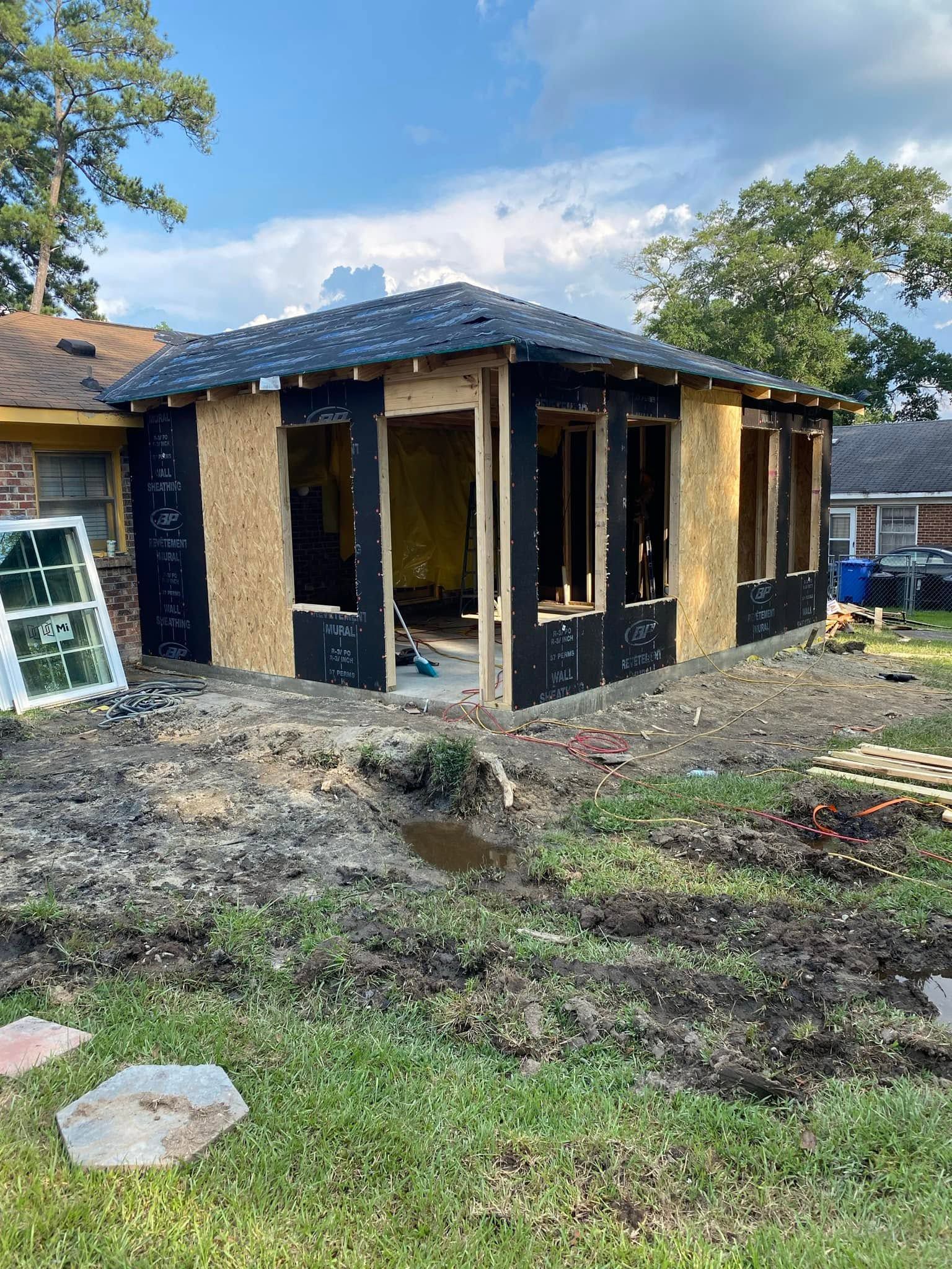 Partially built house with exposed wooden framing and dark exterior wrap in a muddy yard