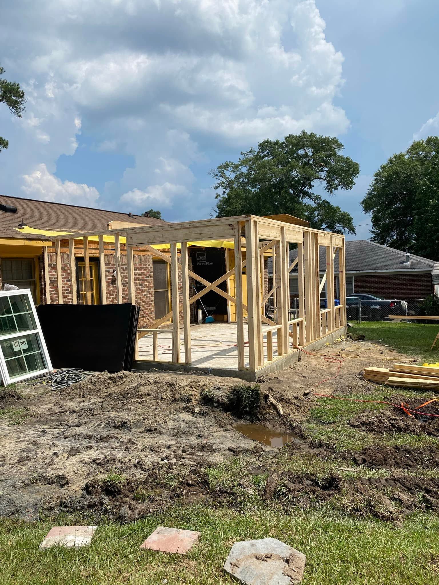 Partially built wooden house frame on a muddy lot under a cloudy sky
