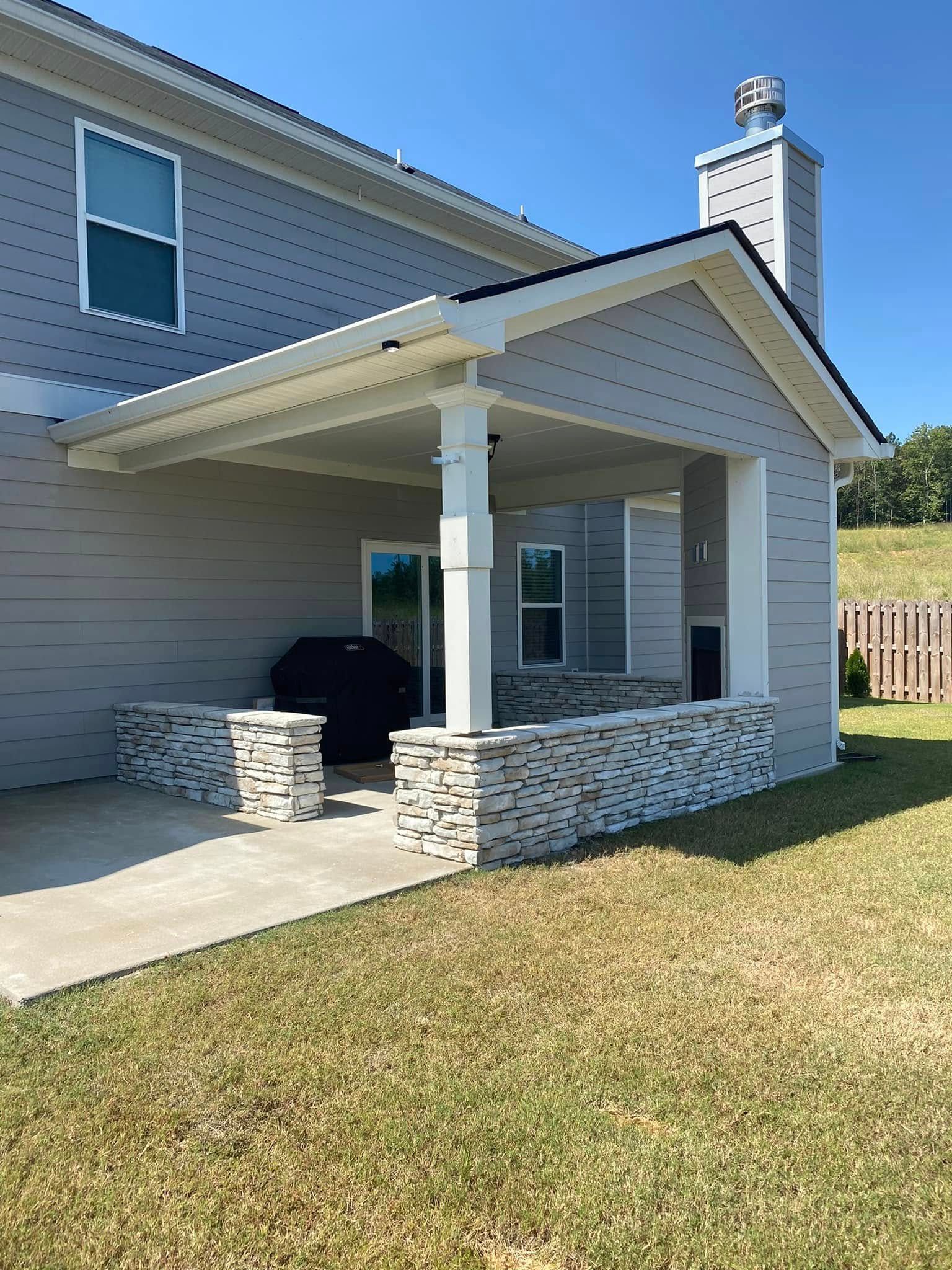 Covered front porch with stone columns on a beige house and a grassy yard.