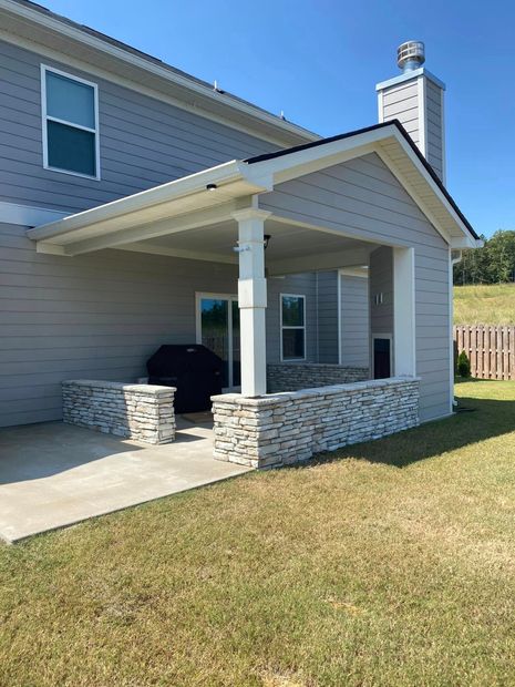 Backyard covered patio with stone half walls and chimney beside a two-story house