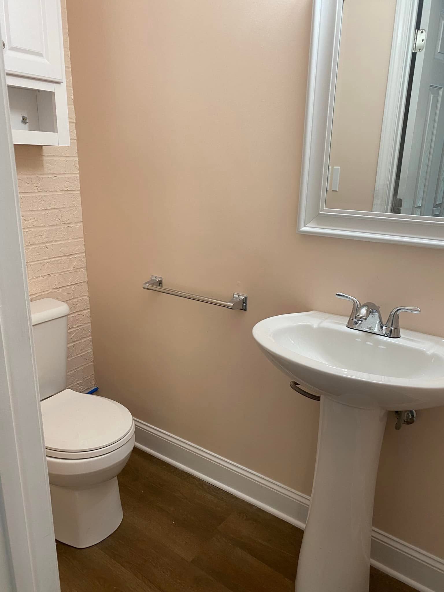 Small bathroom with toilet, pedestal sink, towel bar, and beige walls with wood-look flooring