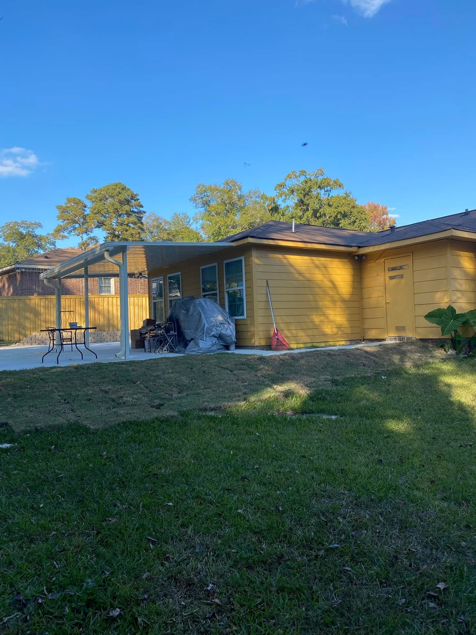 Backyard with a yellow house, screened porch, trees, and a grassy lawn under a clear blue sky