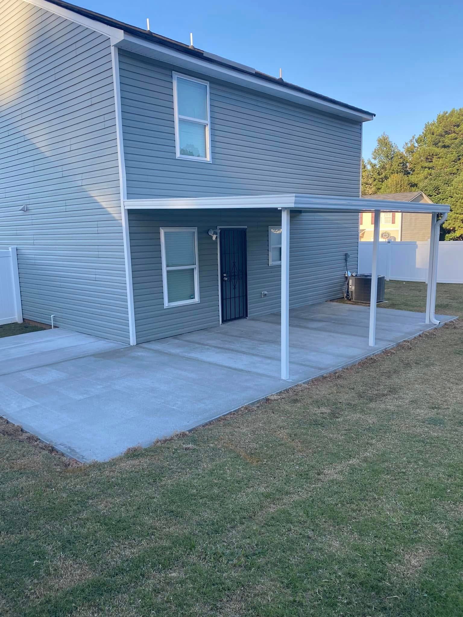 Two-story gray house with a covered concrete patio and white posts beside a grassy yard.