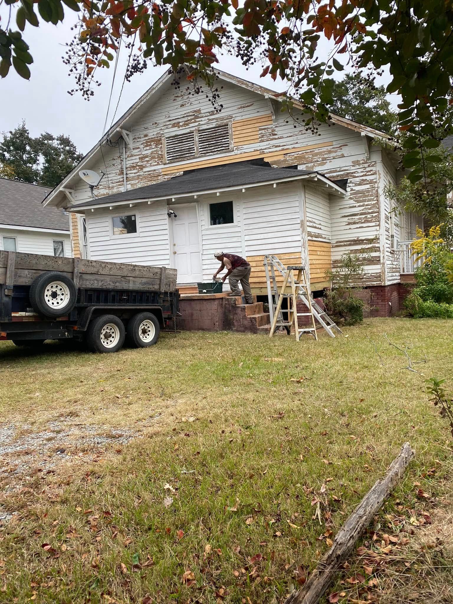 Two workers repair storm damage on a house roof beside a truck and ladder in a yard