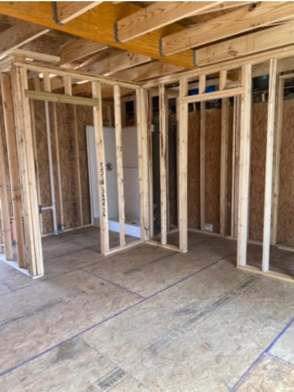 Framed interior of a house under construction with exposed wooden studs and plywood subfloor.