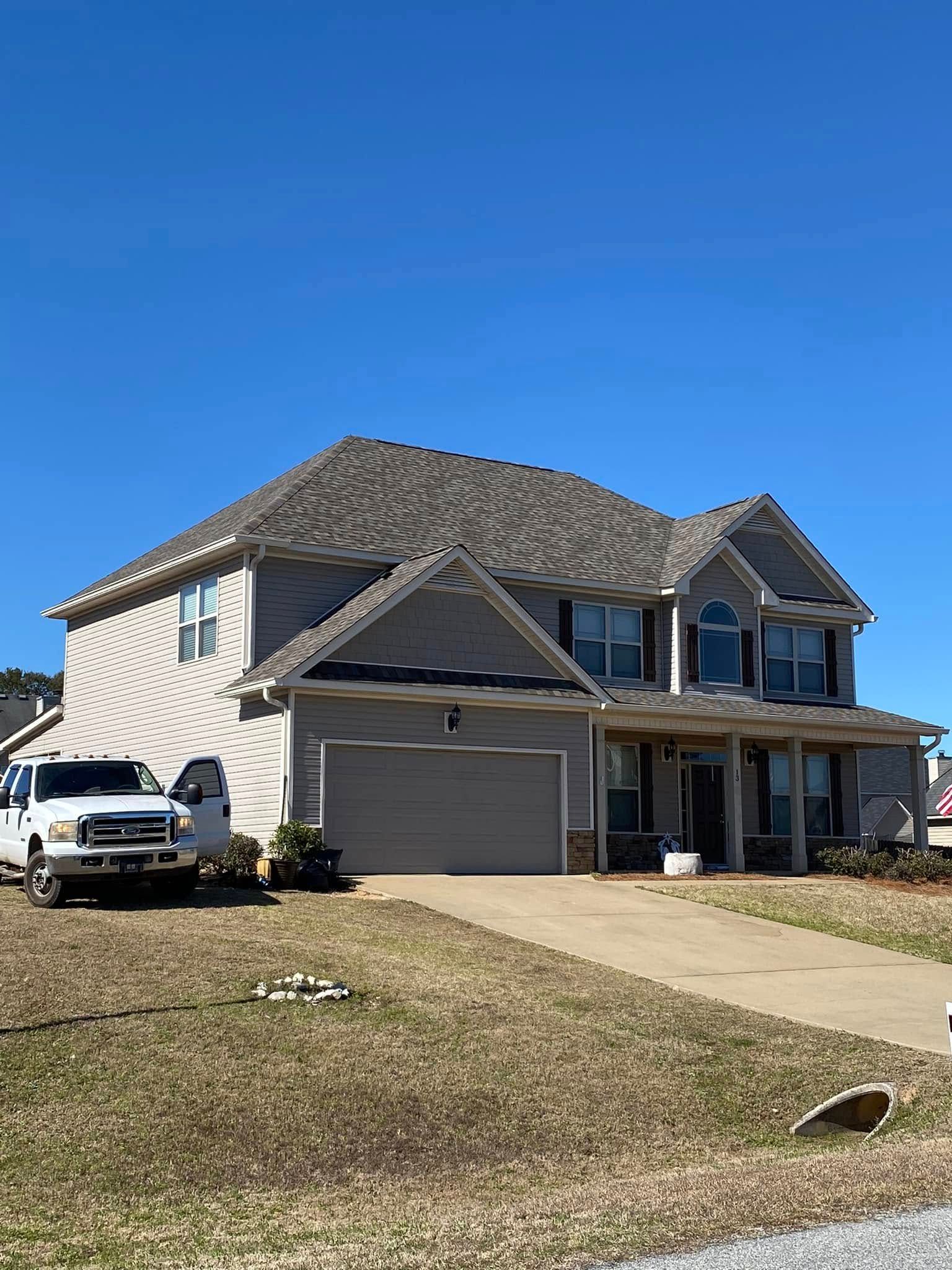 Two-story suburban house with gray roof, white siding, and a driveway under a clear blue sky.