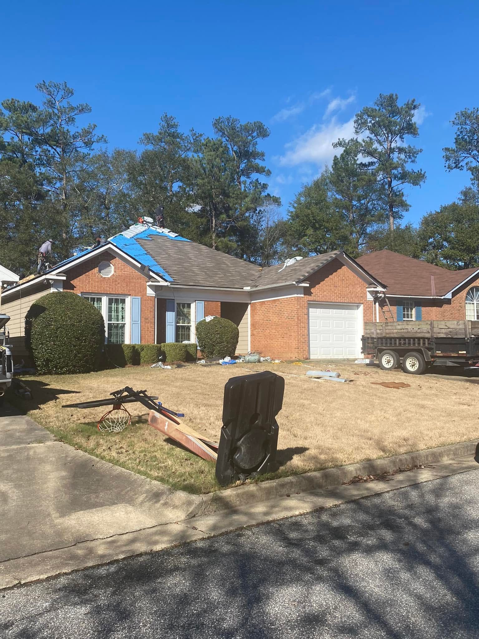 Brick house with damaged roof and front yard debris under a clear blue sky