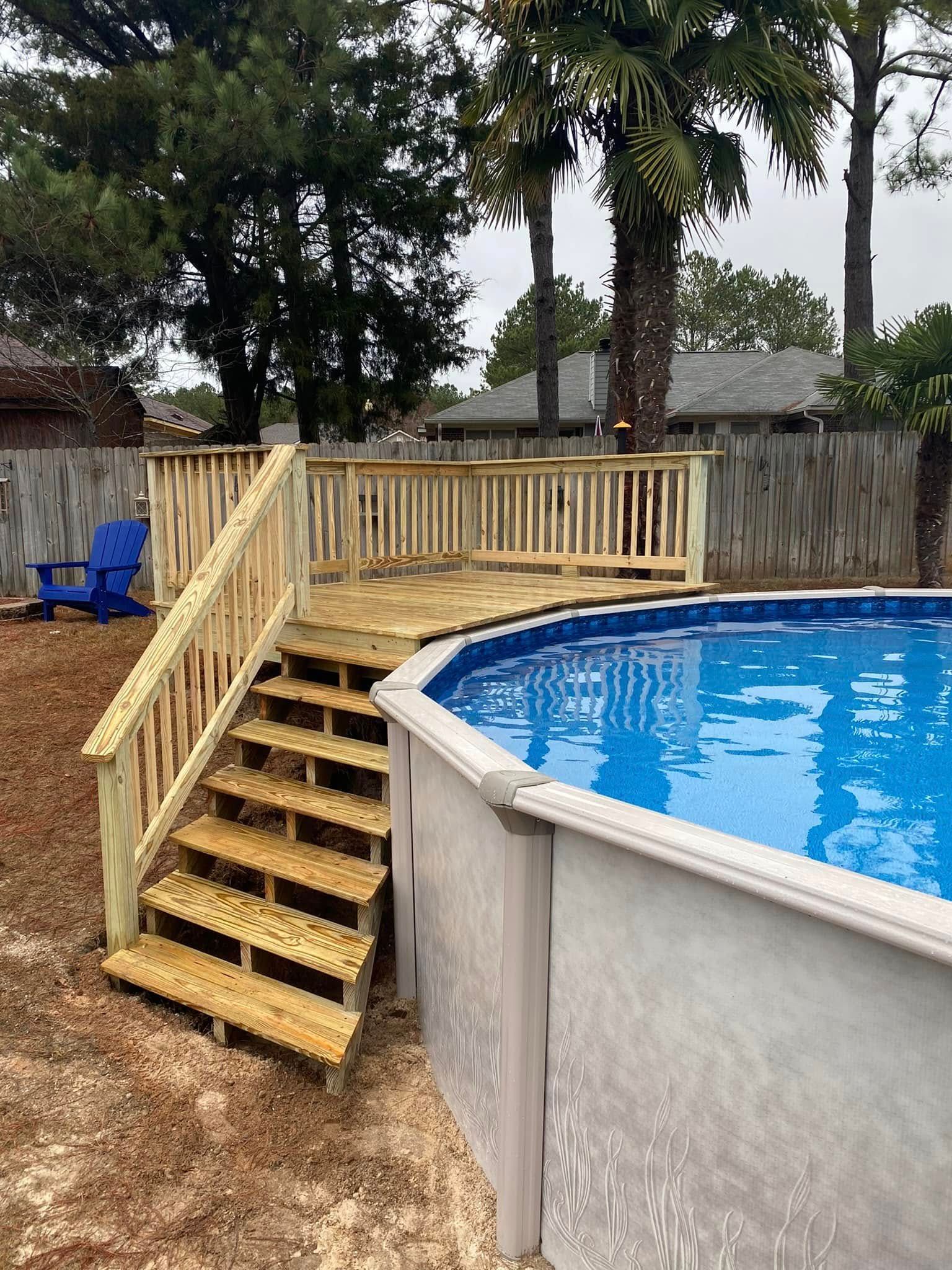 Backyard above-ground pool with wooden stairs and railing, trees and fence in the background