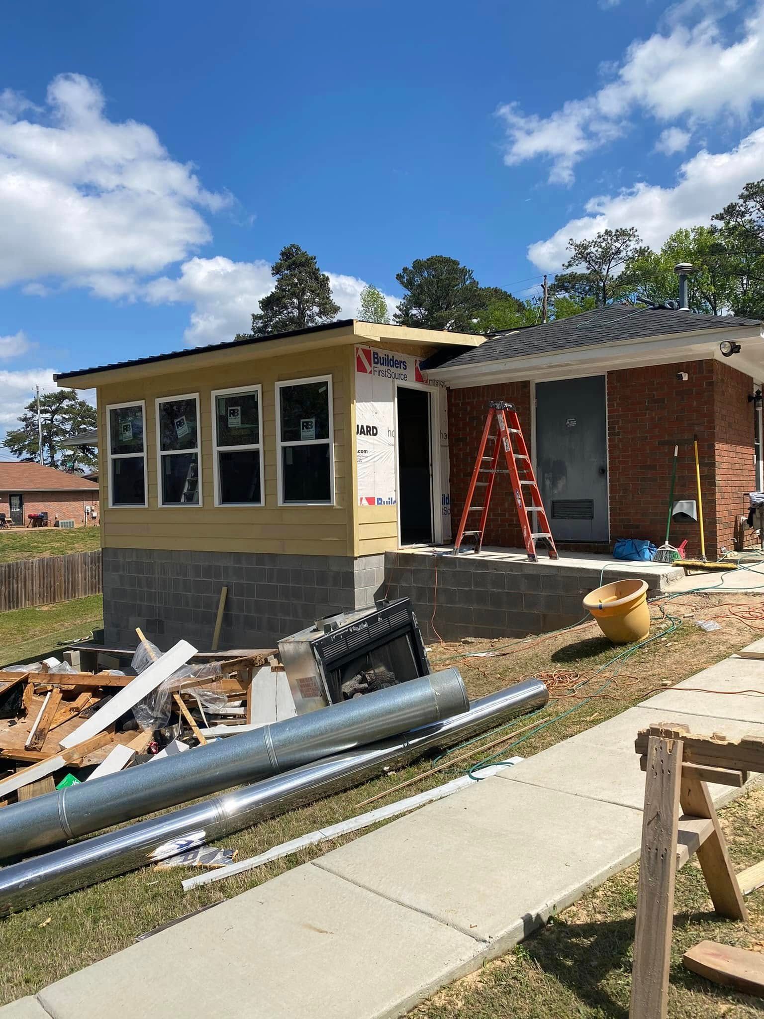 House under construction with yellow siding, red ladder, and building materials scattered outside under a blue sky.