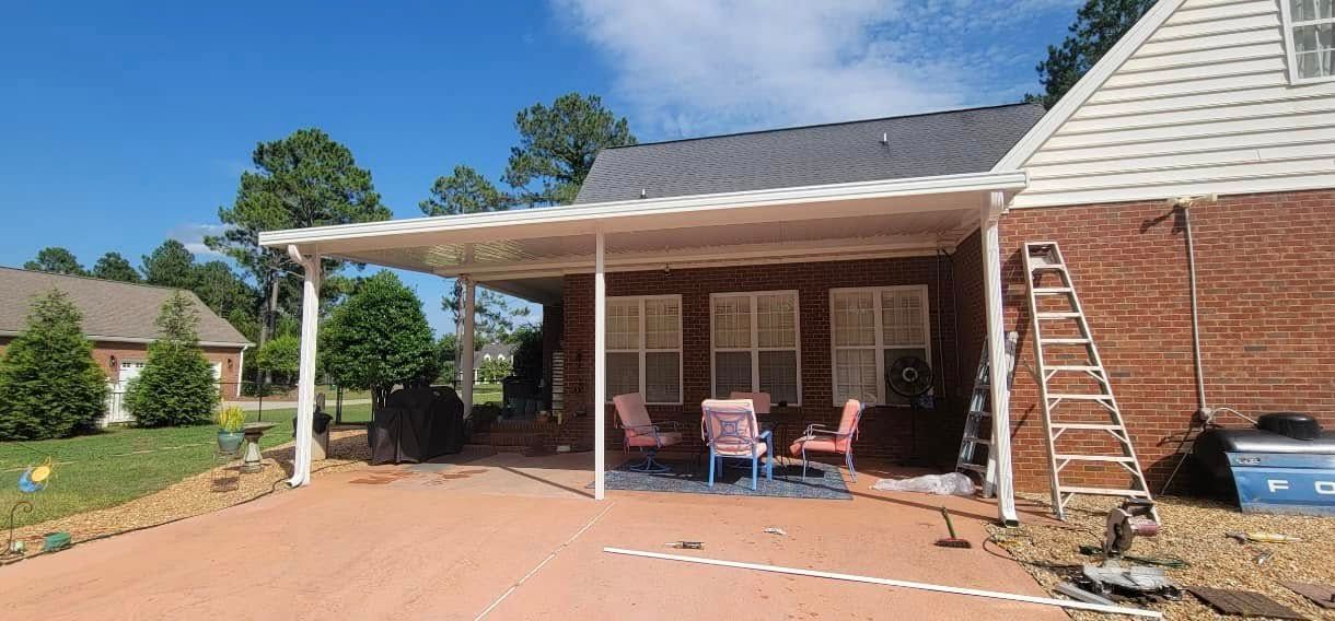 Brick house patio with white awning, pink chairs, and a brick driveway on a sunny day