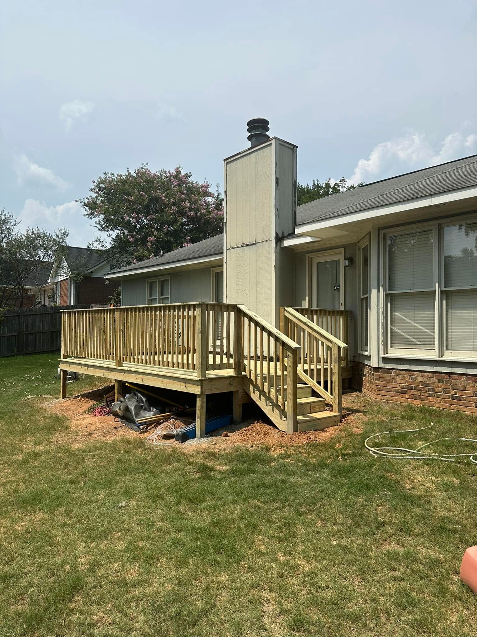 Rear deck with wooden steps and railing attached to a beige house under a partly cloudy sky