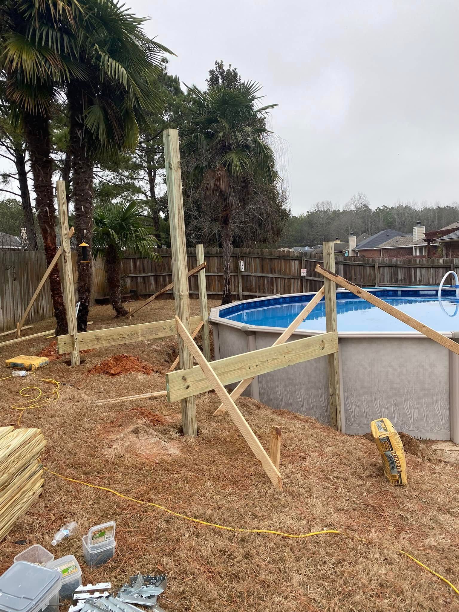 Backyard construction site with a blue above-ground pool, wooden supports, gravel, and trees nearby