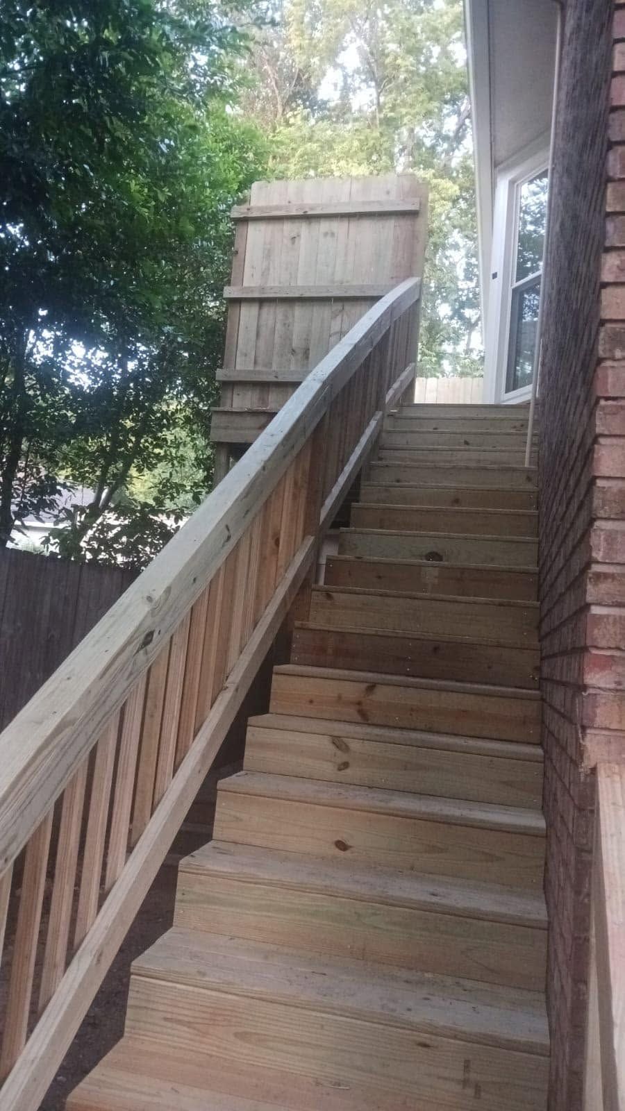 Wooden outdoor staircase with railing leading up beside a house, partly shaded by trees