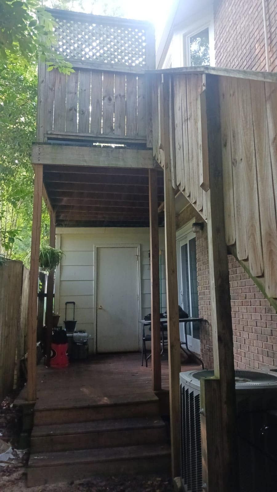 Narrow backyard stairway and wooden upper deck beside a brick wall, with a white door below.