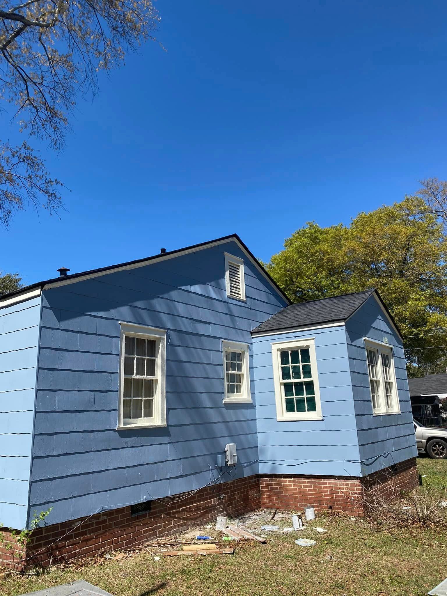 Blue house exterior with white-trimmed windows, brick foundation, and a clear sky above