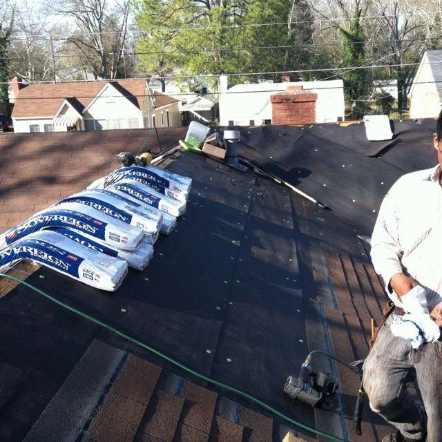 Roofers installing shingles on a sloped roof, with stacks of roofing materials and tools visible.
