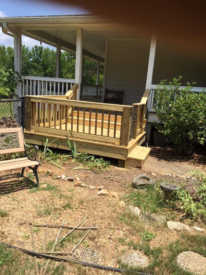 Small wooden porch with railing and steps on a house, viewed from a dry yard with a chair nearby