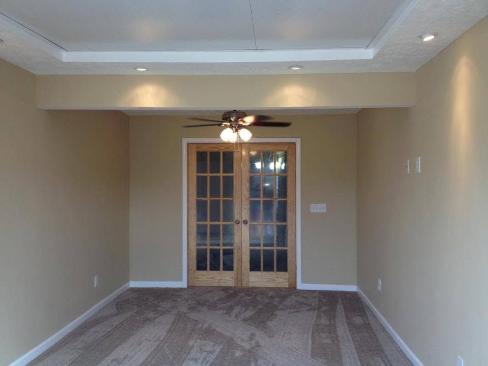 Empty beige living room with carpet, tray ceiling, ceiling fan, and French doors at the far end