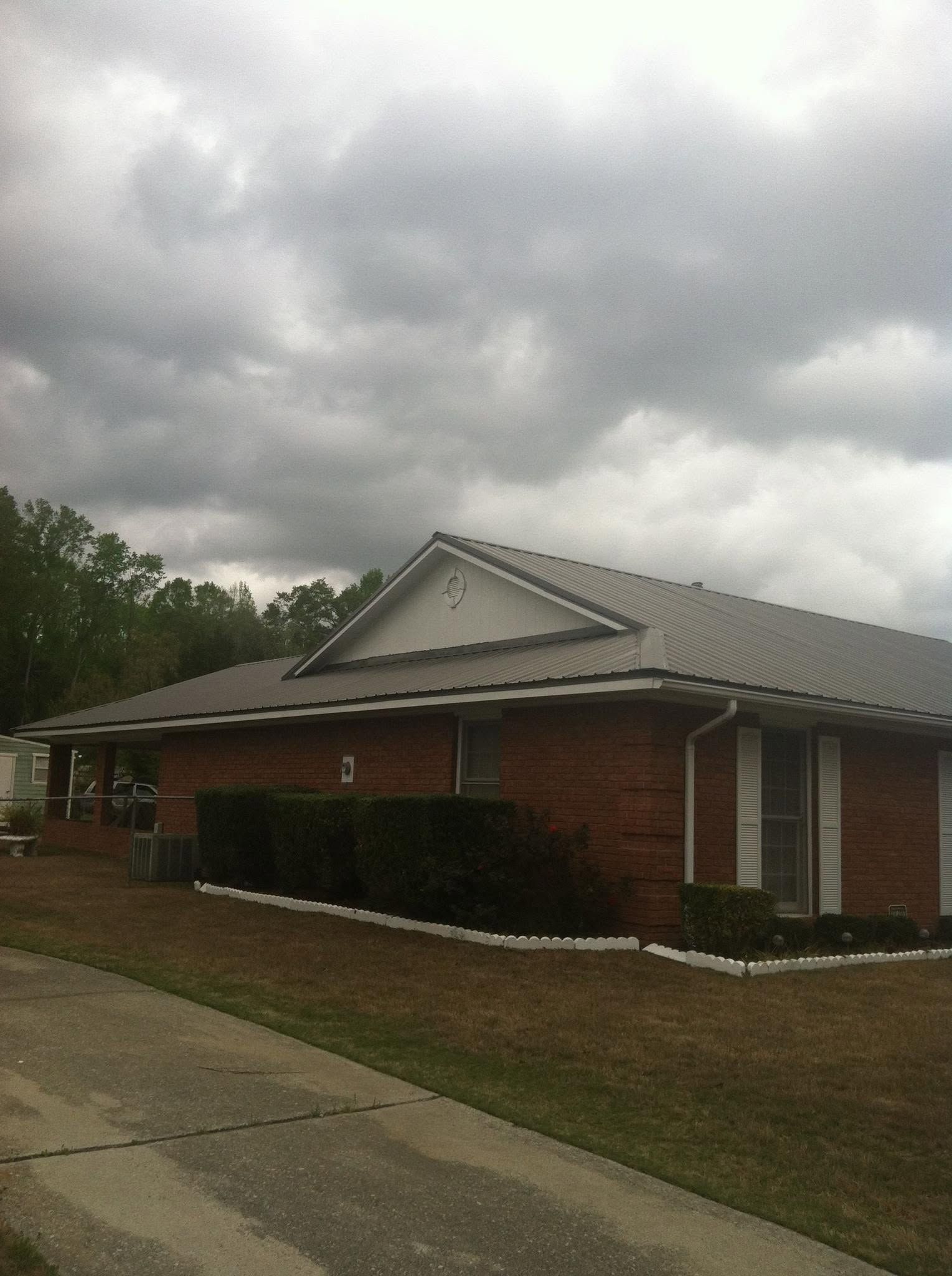 Brick house with a gray roof under cloudy skies beside a sidewalk and lawn