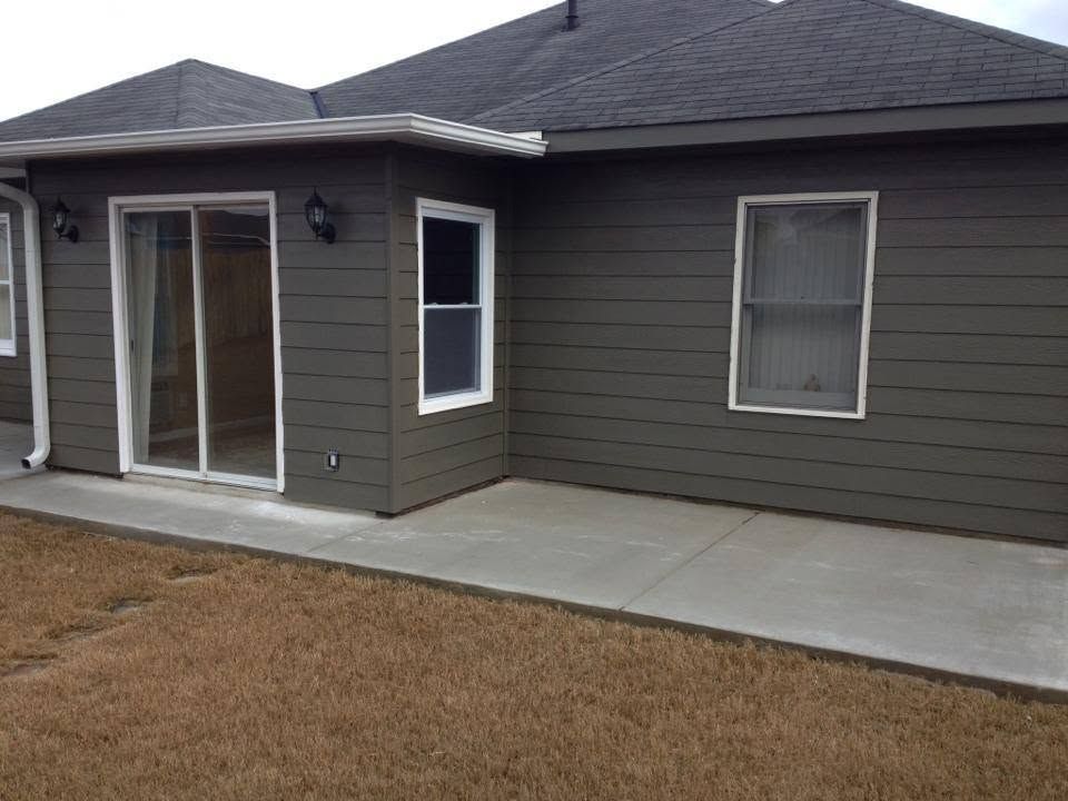 Backyard view of a gray house with sliding glass door, windows, and a concrete patio
