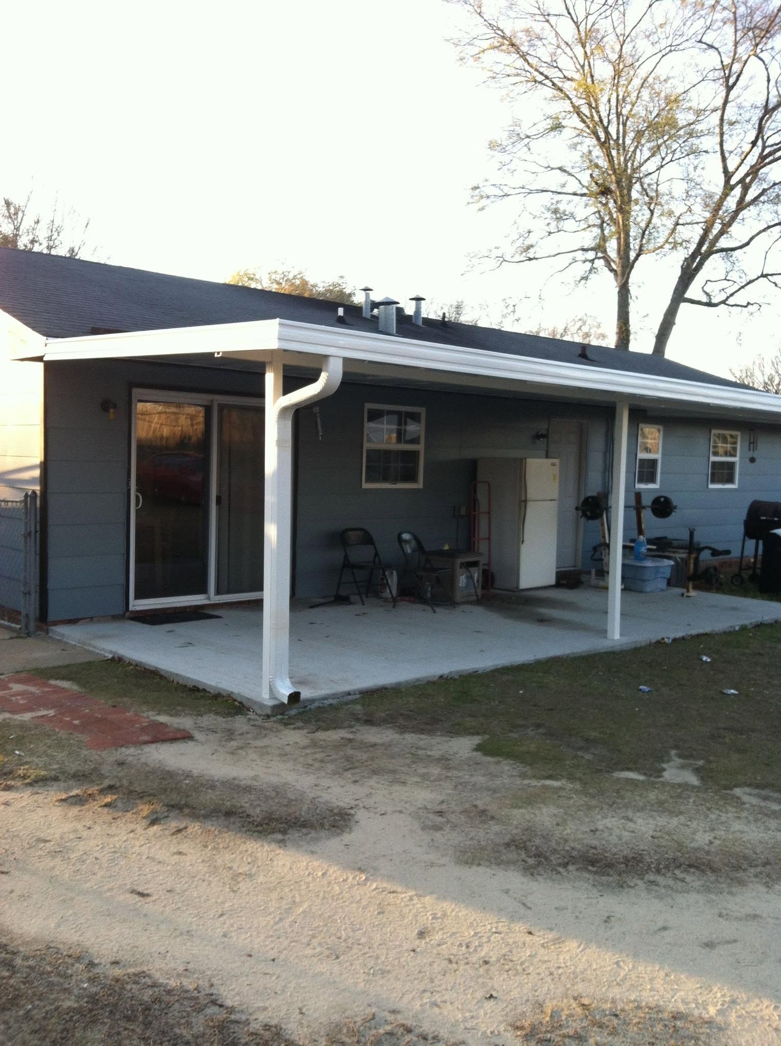 Small gray house with a covered front porch, white posts, and two chairs by the entrance.