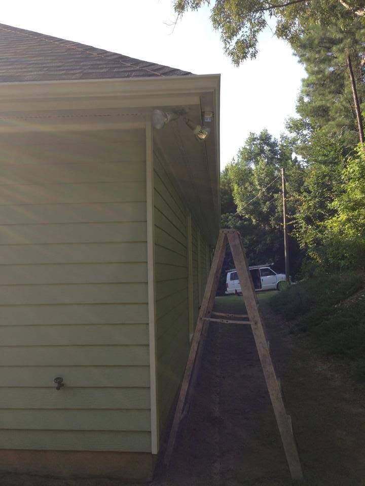 Side of a house with a wooden ladder leaning against the roof edge in a narrow driveway.