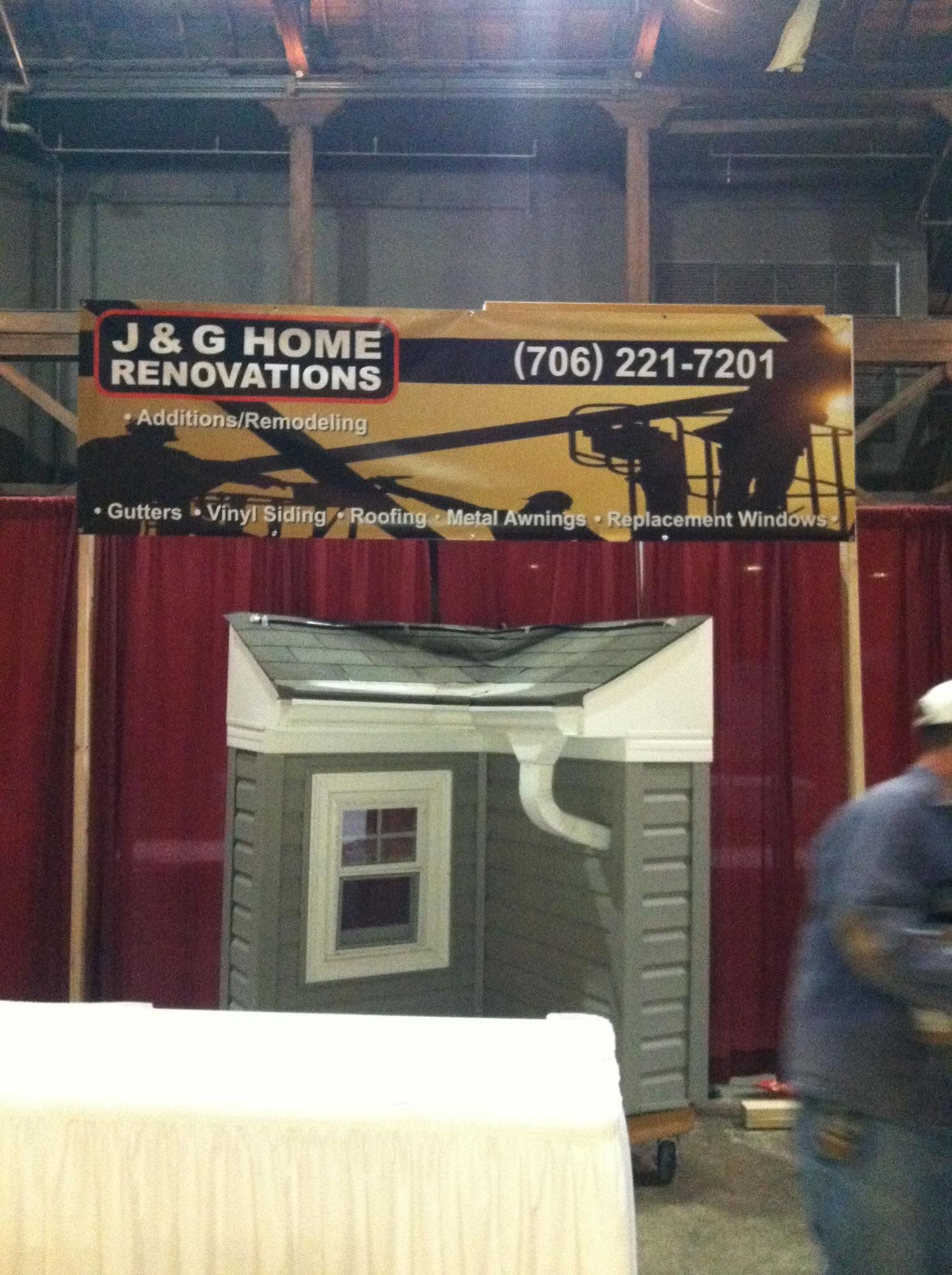 J & G Home Renovations booth with red curtains, house display, and banner showing phone number 706-221-7201