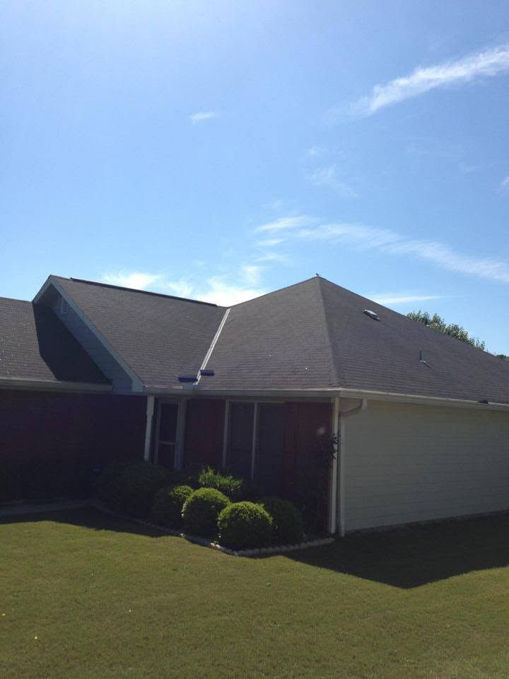 Single-story house with gray roof, beige siding, and a small front lawn under a blue sky