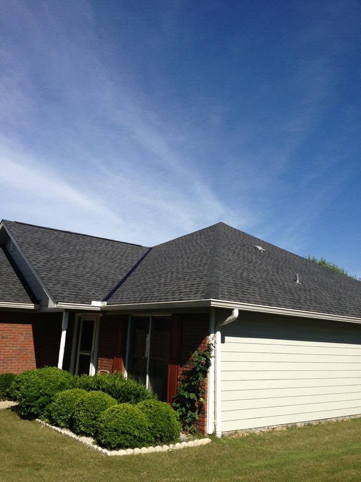 Single-story brick house with dark roof, white garage, and trimmed shrubs under a blue sky