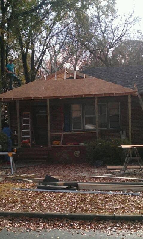 Small brick house with a brown roof, trees behind it, and fallen leaves covering the yard.