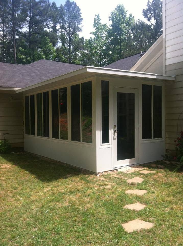 Screened porch addition with white trim beside a house, bordered by trees and a stepping-stone path.