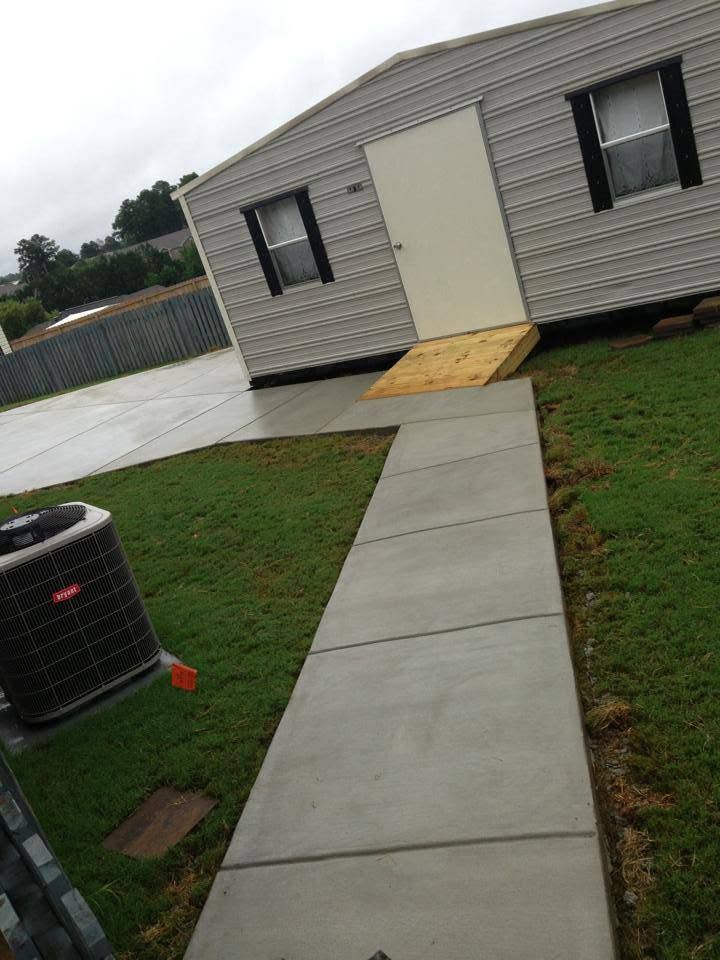 Concrete walkway leading to a portable building entrance with a small wooden ramp over grass