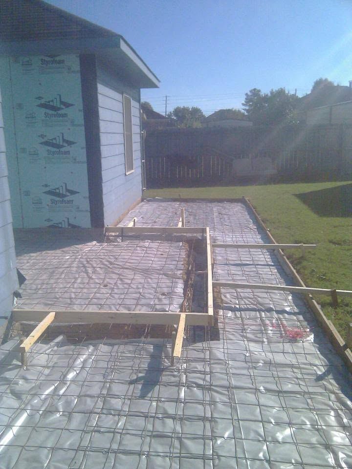 Construction site with concrete forms and rebar beside a house in a sunny backyard