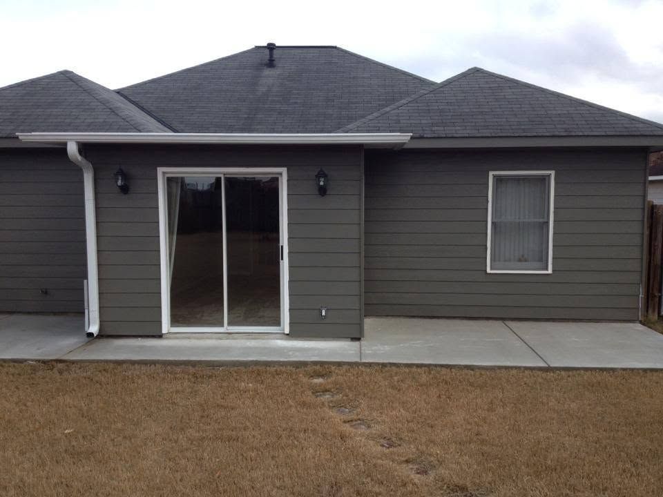 Backyard view of a gray house with sliding glass doors, a small window, and concrete patio.