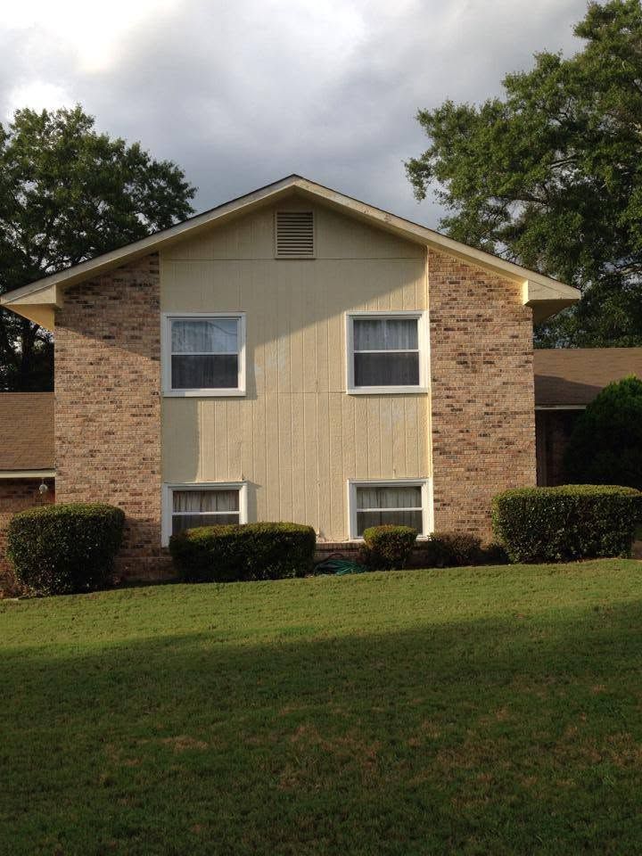 Two-story tan brick apartment building with white-trimmed windows and a grassy lawn