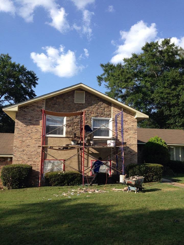 Two workers on scaffolding painting the front of a brick house under a blue sky